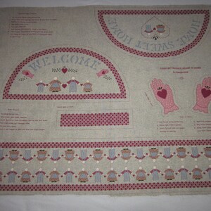May include: A beige fabric panel with instructions for a craft project. The panel features a welcome sign, a pair of pink gloves with hearts, and a border of people holding hands. The text on the panel reads "COUNTRY COTTAGE HEART IN HAND by AMBERTEX".