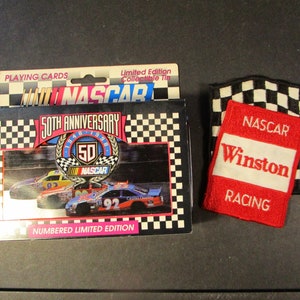 May include: A collectible tin of NASCAR playing cards celebrating the 50th anniversary of NASCAR. The tin features a checkered flag design and a picture of two race cars on the track. The tin also includes a red and white NASCAR Winston Racing patch.