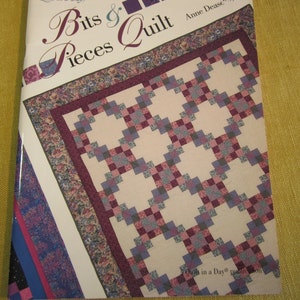 May include: Book cover for "Bits & Pieces Quilt" by Anne Dease. The cover features a quilt with a white background and a pattern of squares in shades of purple, pink, and gray. The text "Quilt in a Day" is visible at the bottom of the cover.