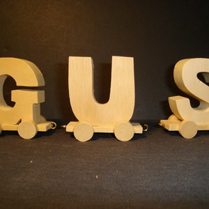 May include: Wooden toy train with three cars, each featuring a large, cutout letter. The cars spell out the name "GUS".