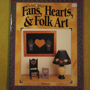 May include: Book cover with the title "Fans, Hearts, & Folk Art" by Jean Wells. The cover features a picture of a framed piece of folk art with a heart and hands, a small chair, a lamp with a heart and birds, and a small card.