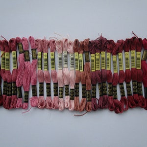 May include: A collection of embroidery floss in various shades of pink and red. The floss is neatly bundled with labels, showcasing a range of colors from light blush to deep burgundy. Ideal for cross-stitch and embroidery projects.