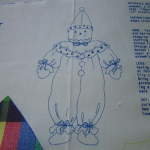May include: A blue line drawing of a clown doll pattern on white fabric. The pattern includes instructions for sewing the doll, including the arms, legs, and hat. The text includes the words "Materials Needed", "Instructions", "Arms", "Legs", and "Hat".