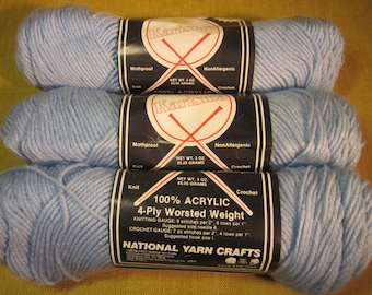 May include: Three skeins of light blue 100% acrylic 4-ply worsted weight yarn. The yarn is labeled "Karisma" and is mothproof and non-allergenic. The label also includes knitting and crochet gauge information.