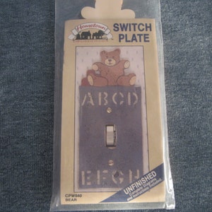 May include: A decorative switch plate with a bear design. The plate is dark blue with the letters A, B, C, D, E, F, G, and H stenciled on it. The top of the plate features a brown bear. The package reads "SWITCH PLATE" and "UNFINISHED".