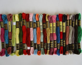 May include: A collection of 24 DMC embroidery floss spools in various colors, including red, blue, green, brown, and yellow. Each spool has a black label with white text indicating the DMC color number.