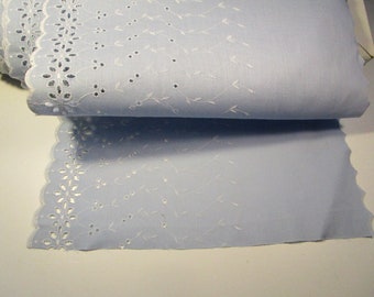 May include: A roll of light blue fabric with white floral and vine embroidery along one edge. The fabric has a scalloped edge with cut-out floral designs. The embroidery features small flowers and delicate vines with tiny dots.