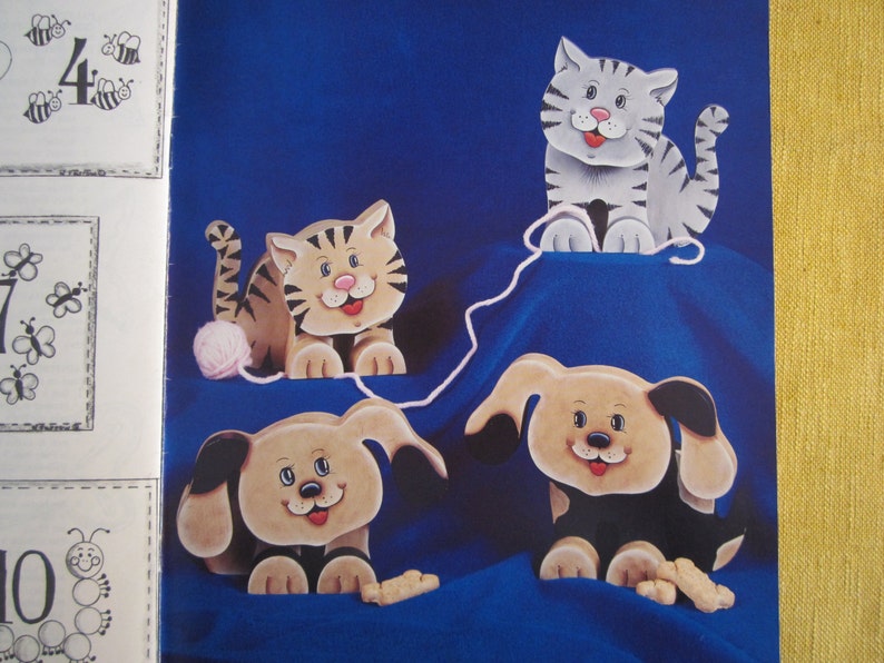 May include: Four wooden animal figurines, a cat, a tiger, and two dogs, are arranged on a blue background. The cat and tiger are playing with a ball of yarn. The dogs are playing with a bone.