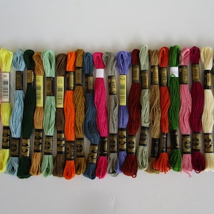 May include: A collection of 25 embroidery floss spools in various colors, including pink, yellow, green, blue, red, orange, brown, and white. Each spool has a black label with gold lettering and a barcode.