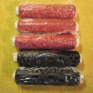 May include: Six spools of metallic thread, four are red and two are black. The spools are wrapped in clear plastic.
