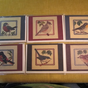 May include: Six cards with embroidered images of different birds on a beige background. Each card has a red, blue, or brown border.