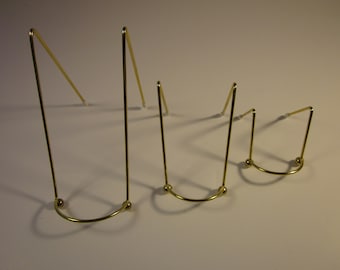 May include: Three gold metal bookends of different sizes. Each bookend has a rounded base and three legs.