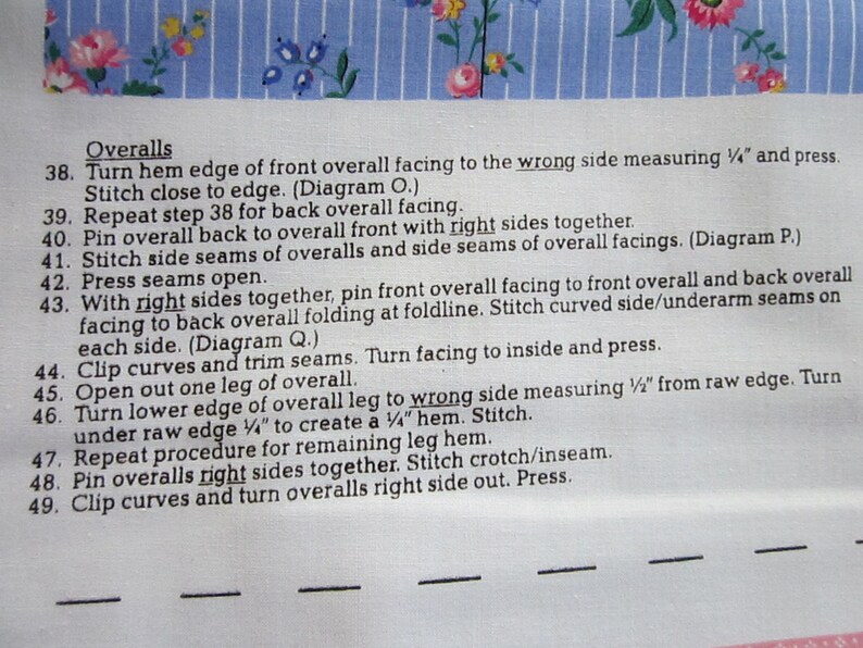 May include: A close-up of a sewing pattern for overalls. The instructions include steps for sewing the side seams, pressing seams open, and turning the hem edge of the front overall facing to the wrong side measuring 1/2 inch.