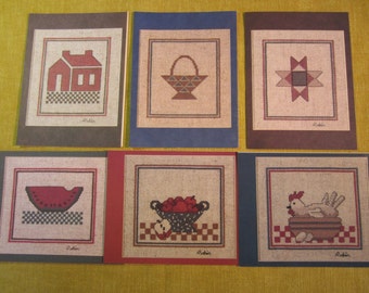 May include: Six cross-stitch patterns on cards with brown, blue, and red borders. The patterns include a house, a basket of fruit, a star, a watermelon, a bowl of apples, and a hen.