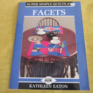 May include: A book titled "Facets" from the Super Simple Quilts series, number 4, by Kathleen Eaton. The cover features a photo of a table setting with two placemats and napkins made with a patchwork quilt design. The placemats are pink, blue, and white with a floral print.