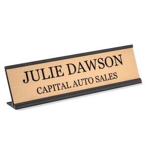 K&ouml;nnte beinhalten: Ein goldenes Schreibtisch-Namensschild mit schwarzer Beschriftung, auf dem "Julie Dawson Capital Auto Sales" steht.