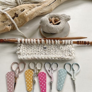 May include: Five pairs of small, decorative scissors with colorful polka dot cases. The scissors are arranged in a row on a white surface.