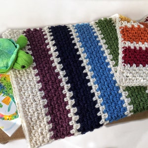 May include: A multi-colored crocheted blanket with stripes of white, purple, navy blue, light blue, green, orange, and red. The blanket is made with a textured stitch and has a fringe border.