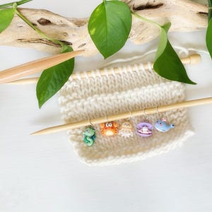 May include: A set of six colourful sea creature stitch markers, including a seahorse, crab, jellyfish, clam, whale, and a knitting needle.