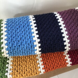 May include: A multi-colored crocheted throw blanket with stripes of green, blue, navy, purple, orange, and red. The blanket has a white crocheted border.