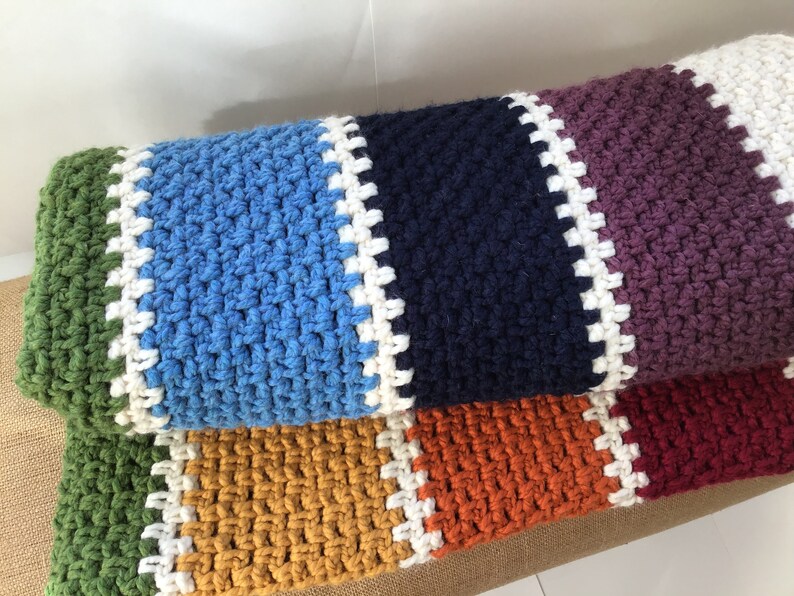 May include: A multi-colored crocheted throw blanket with stripes of green, blue, navy, purple, orange, and red. The blanket has a white crocheted border.