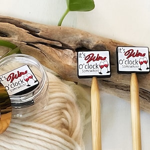 May include: Two wooden knitting needles with black and white square-shaped charms attached to the ends. The charms have the text "It's Wine o'clock Somewhere" and a red wine glass graphic.