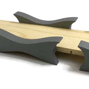 May include: A wooden base with four gray, curved supports. The supports are evenly spaced and appear to be made of a dense material. The wood has a natural, light color. The supports are a medium gray.