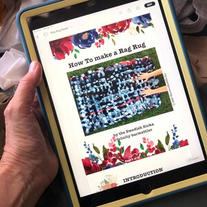 May include: A tablet displays a tutorial titled "How To make a Rag Rug" with floral accents. The tutorial shows a colorful woven rug. The text includes "by the Swedish flicka felicity barmettler" and "Page 2 of 32".
