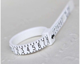 May include: White plastic ring sizer with a numbered scale from 1 to 8. The sizer is adjustable and has a small arrow pointing to the current size.