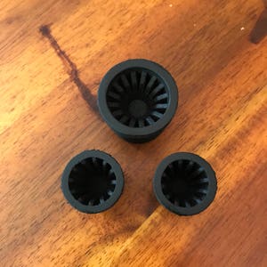 Puede incluir: Tres objetos cilíndricos negros con interior estriado, dispuestos sobre una superficie de madera. Los objetos parecen estar hechos de un material mate, con una abertura circular en la parte superior. Un objeto es más grande que los otros dos.