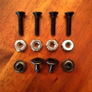May include: An assortment of hardware components, including four black screws, four silver nuts, and three black snap fasteners. The items are arranged on a wooden surface, showcasing their design and construction.