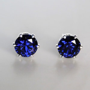 May include: A pair of silver stud earrings with a dark blue gemstone in each. The gemstones are round and have a faceted cut.