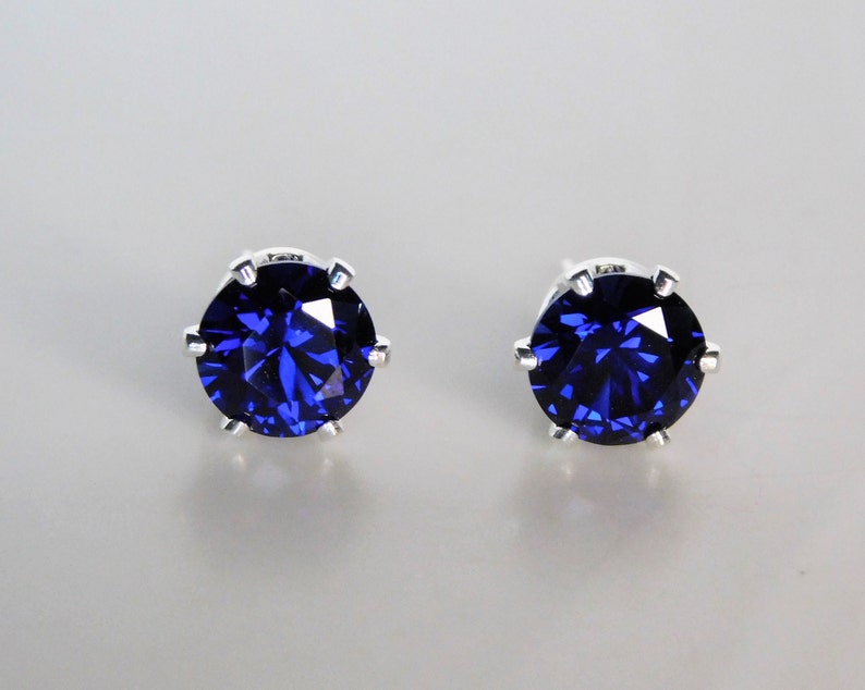 May include: A pair of silver stud earrings with a dark blue gemstone in each. The gemstones are round and have a faceted cut.