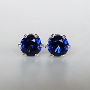 May include: A pair of silver stud earrings with a round, dark blue gemstone in each.