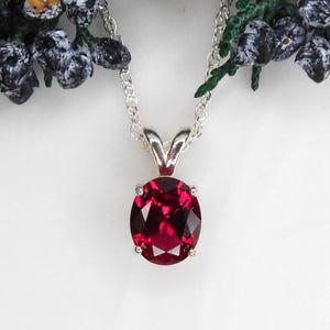 May include: A silver chain necklace with a pendant featuring a large, round, red gemstone.