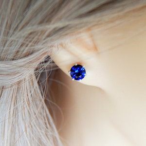 May include: A pair of silver stud earrings with a round, dark blue gemstone.