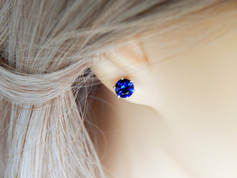 May include: A pair of silver stud earrings with a round, dark blue gemstone.