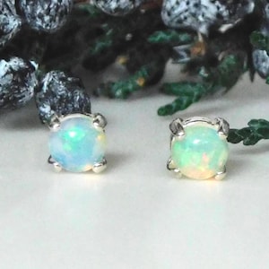 May include: A pair of round stud earrings featuring iridescent white opals set in silver-toned metal prongs. Each opal displays flashes of blue, green, and orange light, secured by four metal claws that hold the circular stones in place.