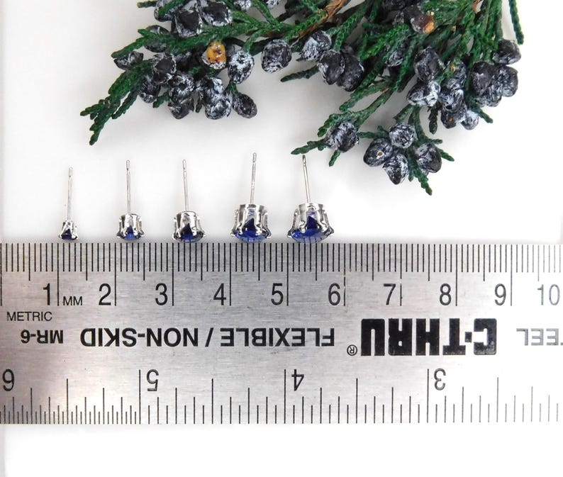May include: Five pairs of silver stud earrings with blue gemstones of varying sizes. The earrings are displayed on a ruler with measurements in inches.