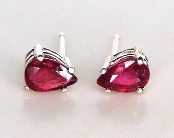 May include: A pair of stud earrings featuring pear-shaped, faceted, deep red gemstones set in silver-colored metal. The earrings have a post and backing for secure wear. The gemstones are the focal point, catching the light.