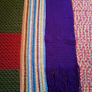 Op de afbeelding: Vier verschillende gehaakte items staan naast elkaar. Links een deken met een groen en rood blokpatroon. Daarnaast een meerkleurige gestreepte sjaal met franjes. Dan een effen paarse sjaal met franjes. Tot slot een neonroze en gele deken met textuur.