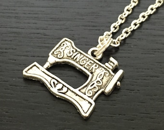 May include: A silver necklace with a sewing machine pendant. The pendant has the word "Singer" engraved on it.