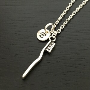 Puede incluir: Collar de plata con un dije de cepillo de dientes y un pequeño dije redondo con la letra E grabada.
