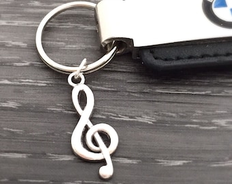 May include: A black leather keychain with a silver metal charm featuring a treble clef. The keychain has a silver metal loop and a silver metal tag with the BMW logo.