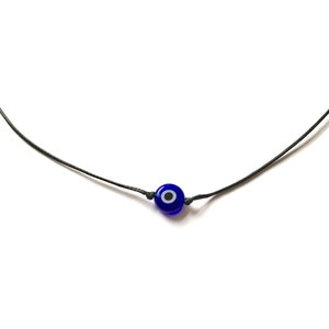 May include: A simple necklace with a blue evil eye charm on a black cord.