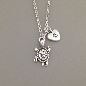May include: A silver necklace with a turtle charm and a heart charm with the letter "E" engraved on it.