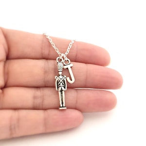 May include: A silver necklace with a charm of a toy soldier and a letter 'J' charm.