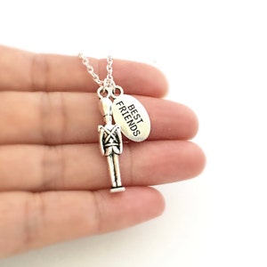 May include: Silver necklace with a toy soldier charm and a silver oval charm that says "Best Friends".