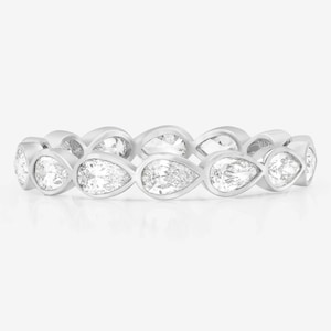 Puede incluir: Un anillo plateado con una serie de piedras preciosas claras en forma de pera, dispuestas en un patrón continuo. Las piedras están espaciadas uniformemente y reflejan la luz. El anillo se presenta sobre un fondo blanco.