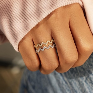 Può includere: Due anelli in oro e argento con un design a zig-zag. Gli anelli sono incastonati con piccole pietre trasparenti.